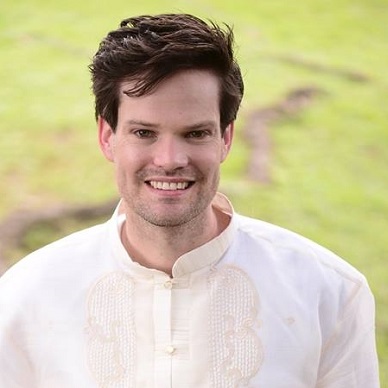 Head shot of Thomas smiling at the camera and wearing a white patterned shirt