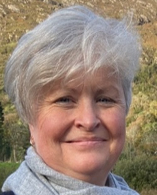 Mary Quirke - a middle aged woman wearing a gray scarf with trees in the background