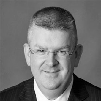 Conor Mc Guckin - a black and white photo of a middle aged man with glasses, wearing a suit