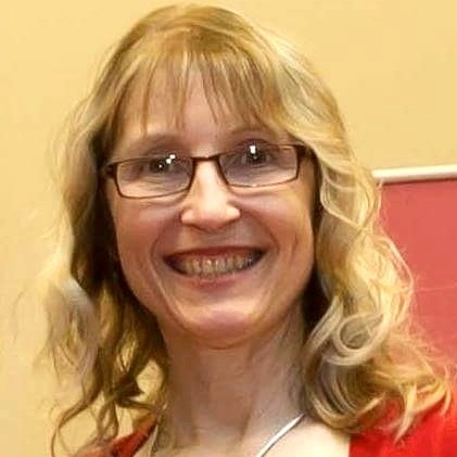 Christine is smiling in her photo. She has curly medium length light brown hair with blonde steaks. She is wearing red glasses and a red cardigan.