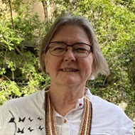 Headshot of Cathy Easte smiling and wearing a white shirt with a necklace of multiple shades of brown beads