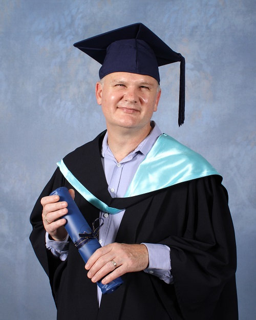 Francois Jacobs wearing graduation robes and holding a rolled up testamur.