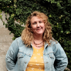 Photo of Riona wearing a denim jacket and yellow top standing in front of a tree