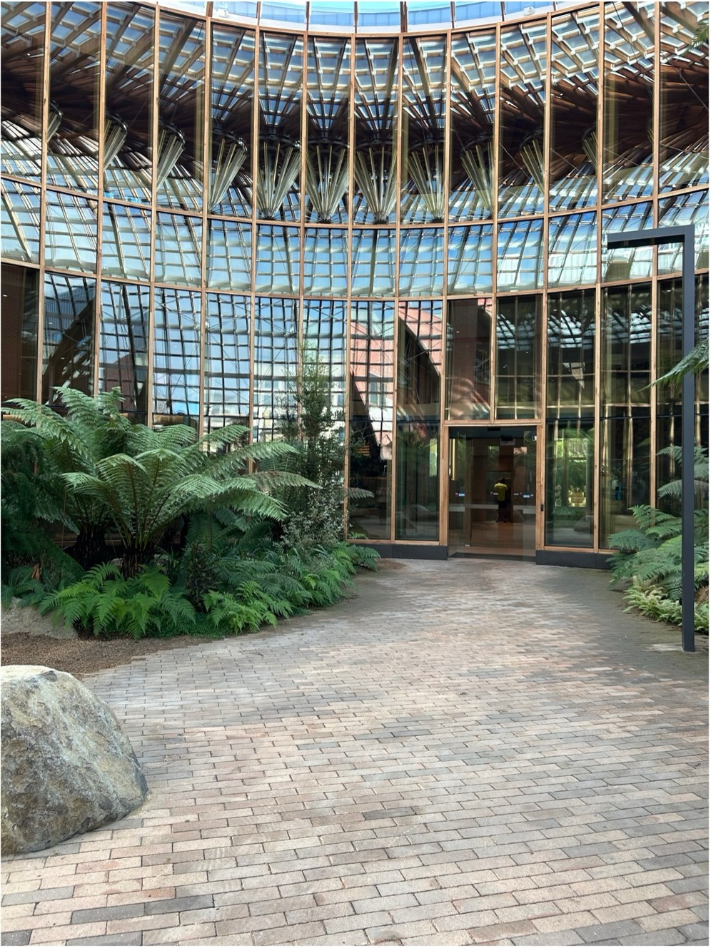 Further into the glass domed building, with a set of glass doors at the end of a gently curved paved pathway. 
