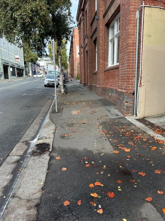 A foot path with a cut-curb on the left-hand side of the view. On the right-hand side is a series of brick buildings, with a gap visible between them. 