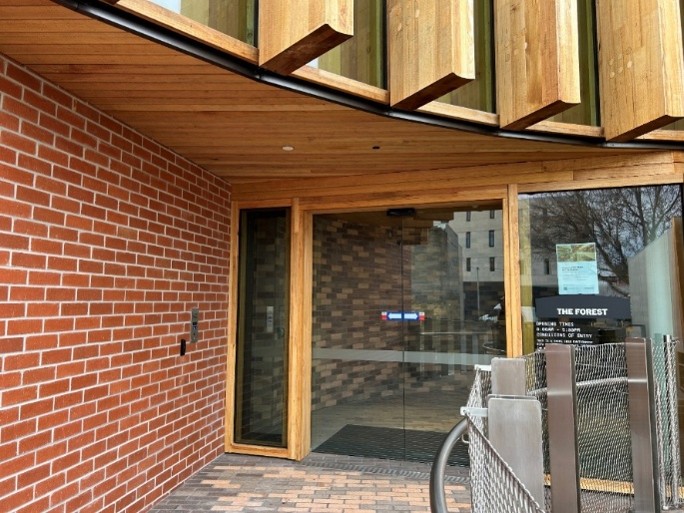 A set of glass sliding doors set into a wooden-panelled building, with a brick wall to the left. 